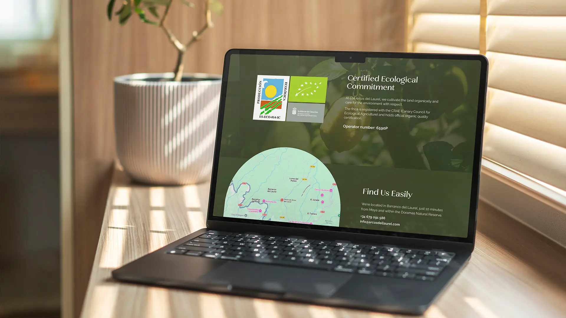 Laptop displaying the Los Arcos del Laurel website, showing ecological certification badges and a location map for Barranco del Laurel