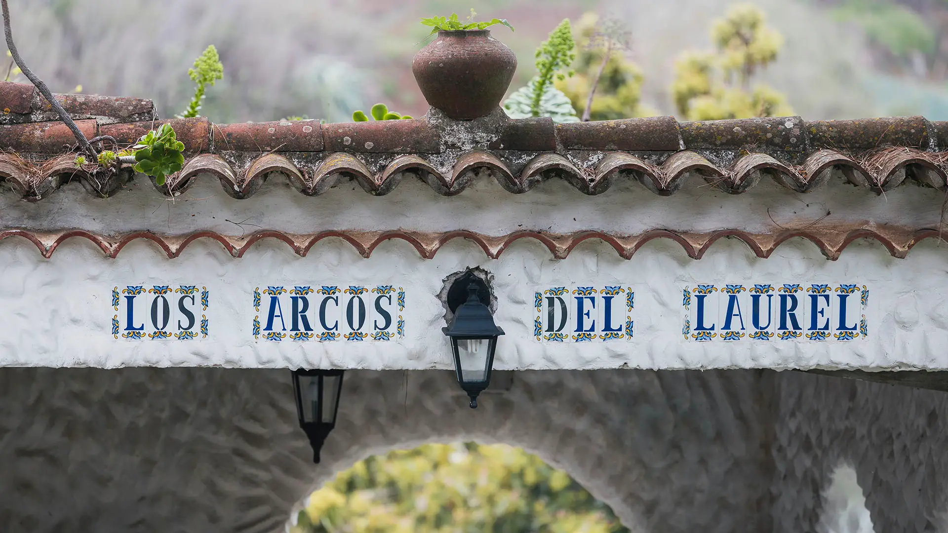 Entrance arch of Los Arcos del Laurel with decorative blue tile lettering, terracotta roof, and hanging lanterns